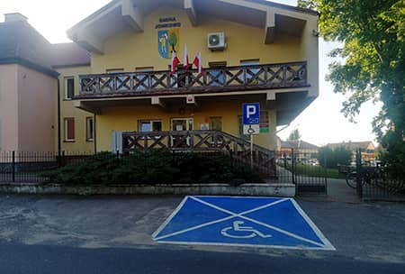 Zdjęcie przedstawiające miejsce parkingowe przed budynkiem urzędu gminy. W tle budynek urzędu.