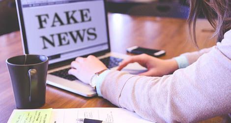 Osoba siedząca przed komputerem na którym wyświetla się komunikat "fake news"
