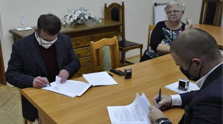 Trzy osoby przy stole. Dwie osoby podpisują dokumenty.