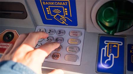 Bankomat, dłoń wpisująca numer na klawiaturze bankomatu.