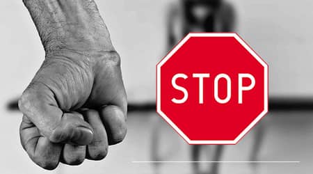 Na pierwszym planie: zaciśnięta dłoń mężczyzny i znak stop; na drugim planie kobieta. 