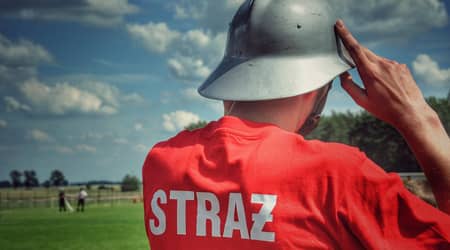 Zdjęcie: salutujący strażak, stojący tyłem, na koszulce napis: straż.