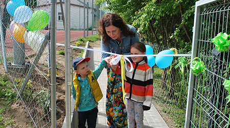 Zdjęcie przedstawiające trzy postaci stojące przy furtce i przecinające wstęgę.