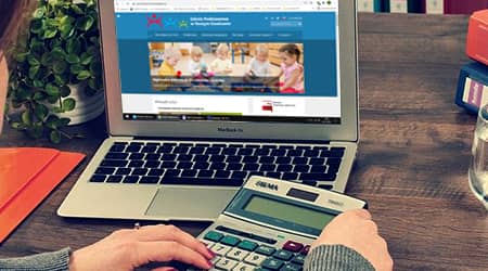 Zdjęcie przedstawiające laptopa stojącego na biurku oraz dłonie osoby obsługującej kalkulator..