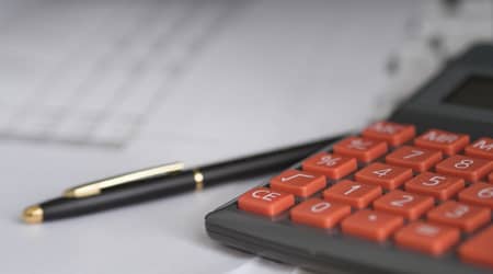 Zdjęcie przedstawiające kalkulator i długopis. W tle stos kartek.