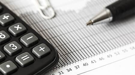 Zdjęcie kalkulatora, długopisu i kartki z tabelami.