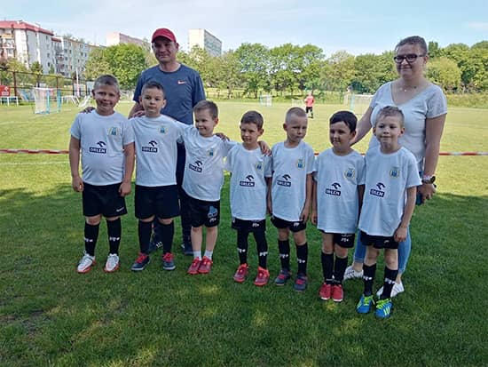 Zdjęcie grupy przedszkolaków w strojach piłkarskich z wychowawcą i trenerem.