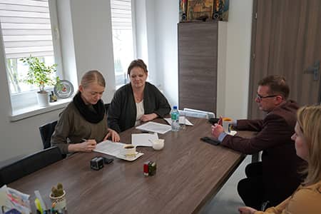 Zdjęcie czterech osób siedzących przy stole:  trzy kobiety i mężczyznę. Jedna z kobiet podpisuje dokumenty.