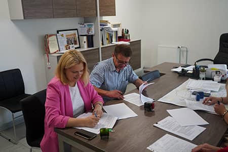 Kobieta i mężczyzna siedzący przy stole podpisują dokumenty.