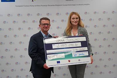 Kobieta i mężczyzna stoją, trzymając w rękach symboliczny czek.