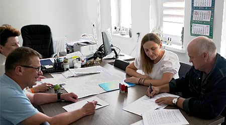 Cztery osoby siedzące przy stole w gabinecie wójta podczas podpisywania dokumentów.