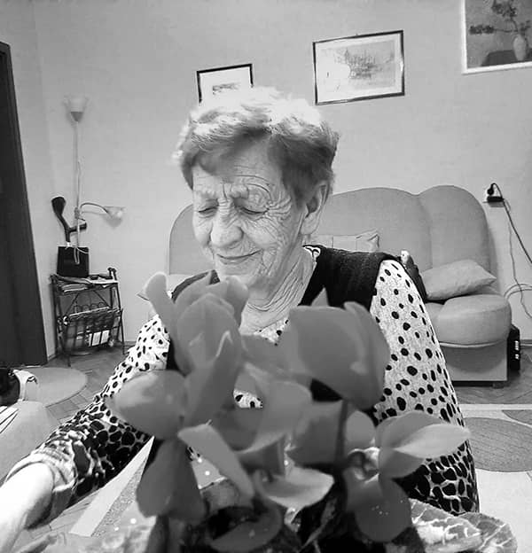 Zdjęcie starszej kobiety siedzącej przy stole, na którym stoi kwiat.