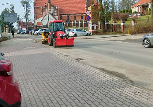 Zdjęcie widoku ulicy po której jedzie traktor z maszyną do zamiatania.