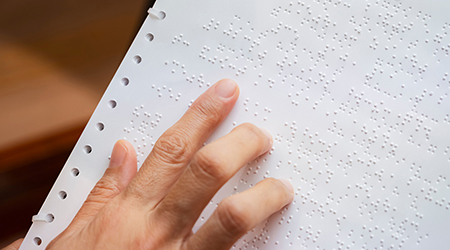Dłoń odczytująca tekst z kartki zapisanej w języku Braille'a