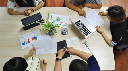 Widok z góry na pięć osób siedzących przy stole i przeglądających dokumenty. 